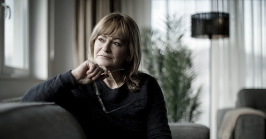 Middle-aged woman with hand under her chin sitting on a couch in thought.
